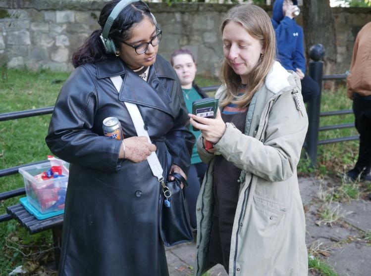 Two people using Our Outdoors on their phone in a local park for the Dear Green Place project